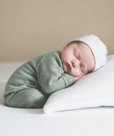 a baby sleeping on top of a white pillow wearing a knitted hat and green sweater