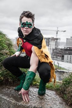 a man dressed in green and black with his hands on the ground, posing for a photo