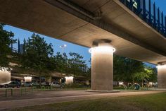 an underpass at night with cars and people on the sidewalk below it, in front of some trees