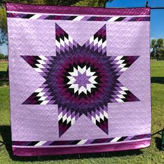 a purple and black quilt is hanging on a clothes line in the grass near some trees