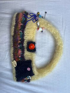 a knitted scarf with buttons and other things on it sitting on top of a white sheet