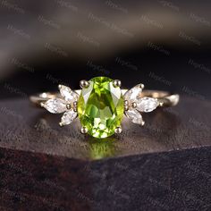 a green ring with three pear shaped diamonds on it's side, sitting on top of a wooden surface