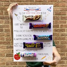 a person holding up a sign with candy bars on it in front of a brick wall