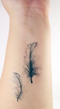 two feather tattoos on the back of a woman's left arm, one is black and white