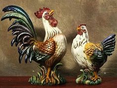 two colorful rooster figurines sitting on top of a wooden table next to each other