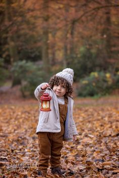 a little boy standing in leaves holding a lantern with one hand and looking at the camera