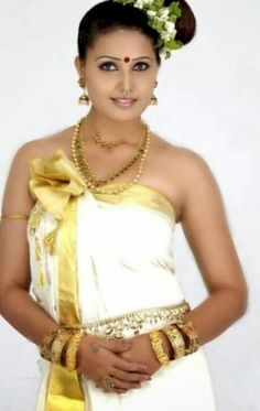 a woman in a white and gold sari with flowers on her head, standing