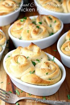 small white bowls filled with baked rolls on top of a wooden table next to a fork