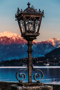 an old fashioned street light with mountains in the backgroung and water below