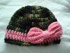 a crocheted hat with a pink bow is laying on a white sheet,