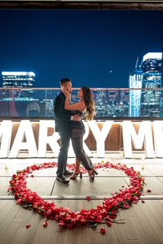 a man and woman standing next to each other in front of a heart