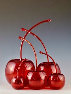 a group of red glass cherries sitting on top of each other in front of a gray background