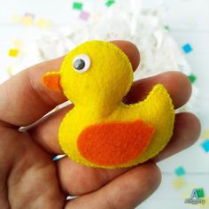 a hand holding a small yellow and orange felt ducky ornament on it's finger