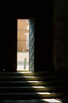 an open door leading into a dark room with stairs and light coming in from it