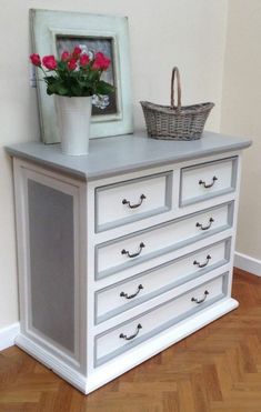 a white dresser with flowers on top and a basket full of pink roses in the bottom drawer