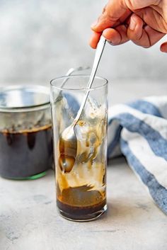 a person is spooning ice into a glass with liquid in it on a table