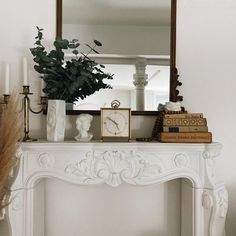 a white mantle with a clock, flowers and candles on it in front of a mirror