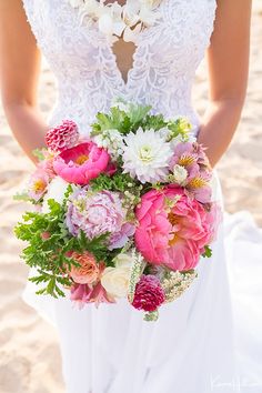 a bride holding a bouquet of flowers on the beach