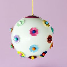 a white ornament with colorful flowers hanging from it's side on a purple background