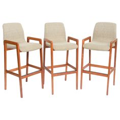 three wooden bar stools with beige upholstered seat cushions and backrests