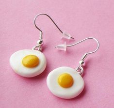 two fried eggs are hanging from earrings on a pink surface