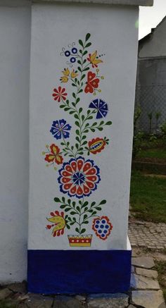 a white and blue building with flowers painted on it's side next to a brick walkway