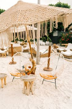 two chairs and an umbrella on the sand at a beach wedding reception in mexico, with tables set up under them