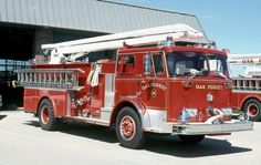 an old red fire truck parked in front of a building with other trucks behind it