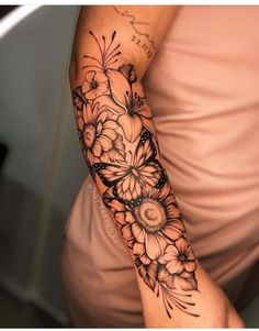 a woman's arm with flowers and butterflies tattooed on the arm, in black ink