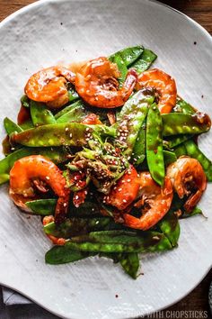 a white plate topped with green beans and shrimp covered in seasoning on top of a wooden table