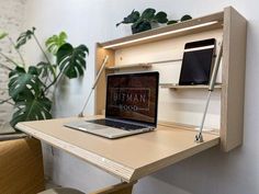 an open laptop computer sitting on top of a wooden desk next to a potted plant