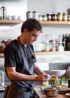 a man in an apron preparing food on top of a wooden cutting board next to a counter