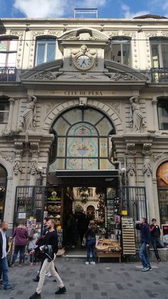 people are walking in front of a building with a clock on it's side