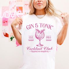 a woman wearing a gin and tonic t - shirt standing in front of a wall