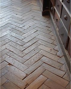 an image of a herringbone floor in the middle of a kitchen with dark wood cabinets