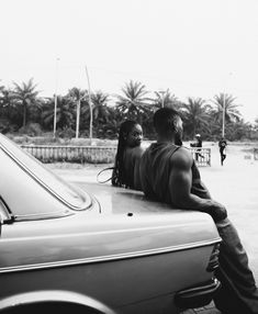 black and white photograph of two people sitting on the hood of a car in a parking lot