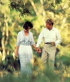 a man and woman holding hands walking through the woods