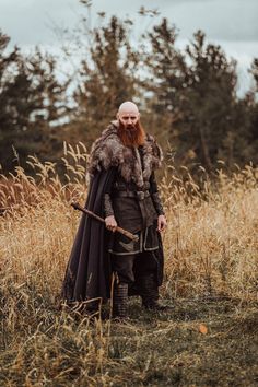 a bearded man with a long beard wearing a fur cape and holding a stick in a field