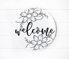 a sign that says welcome with flowers on the front and back of it, against a white background