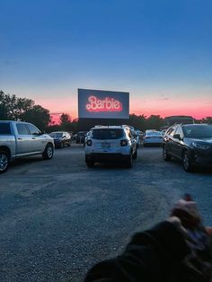 several cars are parked in front of a large billboard with the word barbie on it