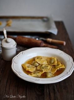 a white plate topped with ravioli next to a bottle of wine and a rolling pin