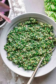 a white bowl filled with spinach and topped with a spoon next to some lettuce