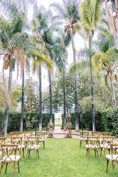 an outdoor ceremony set up with wooden chairs and palm trees