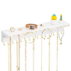 a white shelf with lots of gold jewelry on it and a watch hanging from the top