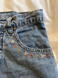 a pair of blue jeans with embroidered flowers on the bottom and side, sitting on a bed