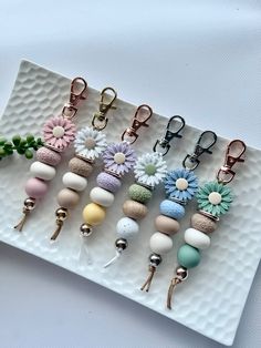 six key chains with flowers on them sitting on a white plate next to a plant