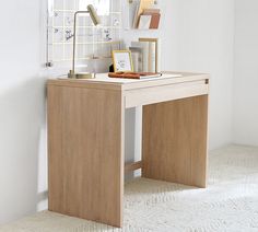 a wooden desk with a lamp and pictures on it in a white walled room next to a window