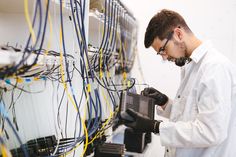 a man in white lab coat and black gloves working on an electrical panel with wires