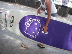 a woman holding a purple hello kitty surfboard