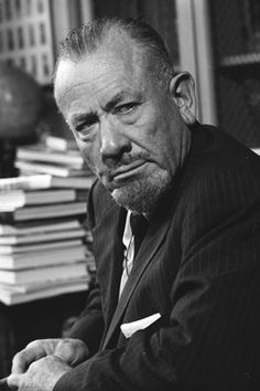 a man sitting at a desk with stacks of books in front of him and looking off to the side